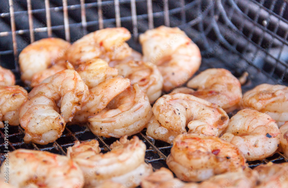 Large mouth watering seasoned wild caught shrimp being grilled over charcoal in a grill basket