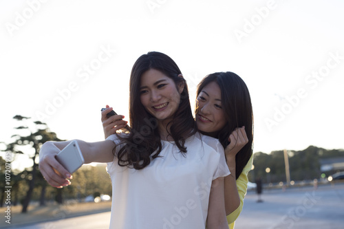 Two young women are taking a commemorative photo with smartphone