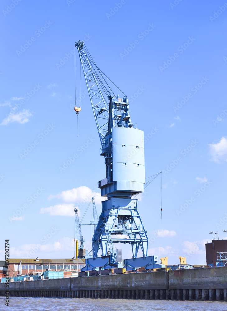 Harbor crane at Hamburg Harbor. Freight shipping equipment, industrial machine. Commercial dock with crane for freight shipping. Shipyard or wharf in the sunlight.