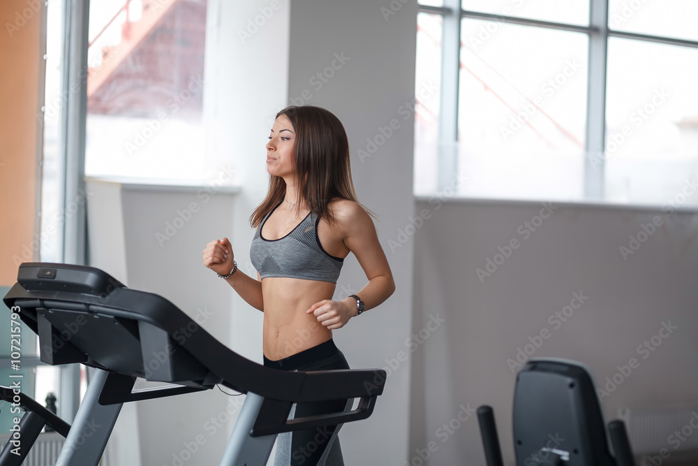 Beautiful young girl engaged in fitness in the gym. He runs on the treadmill. Performs physical exercise. Beautiful young girl engaged in fitness in the gym. He runs on the treadmill. Performs physical exercise.