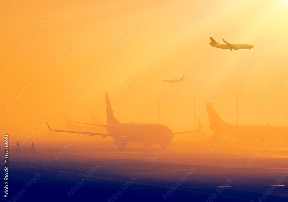 Airport in a foggy weather - silhouettes of airplanes early in the morning. Aircrafts in a fog, international airport at sunrise. Air travel - passenger and commercial transportation. Airport in a foggy weather - silhouettes of airplanes early in the morning. Aircrafts in a fog, international airport at sunrise. Air travel - passenger and commercial transportation.