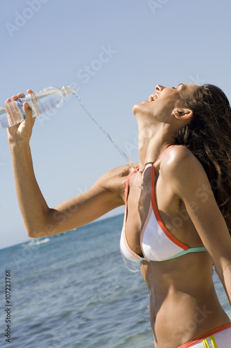 femme en maillot à la mer s'éclaboussant avec une bouteille d'eau