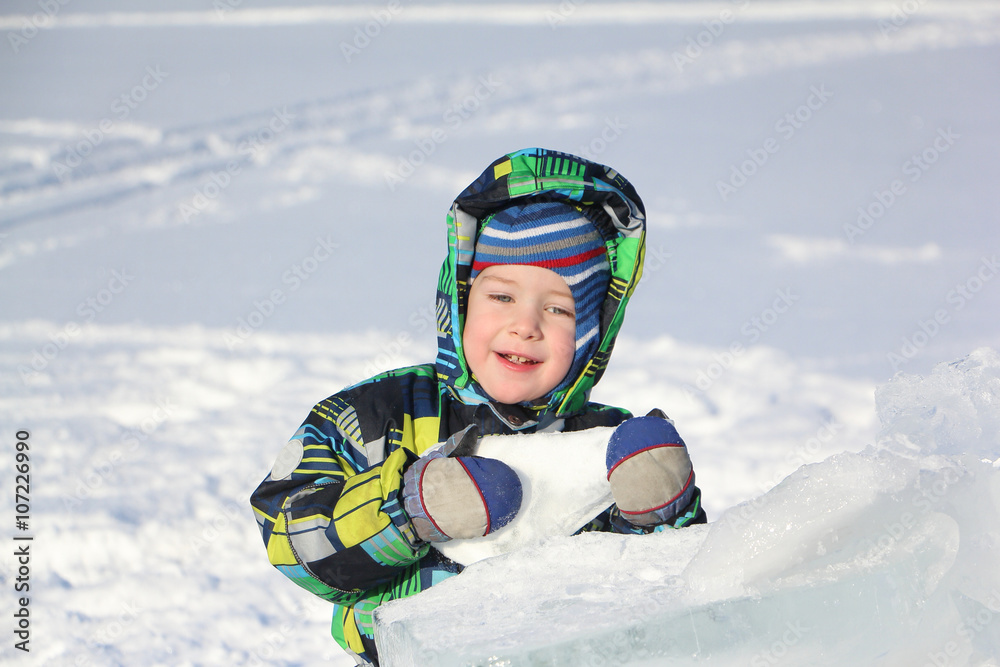 The little boy in a color jacket with a hood the piece of ice holding in hand
