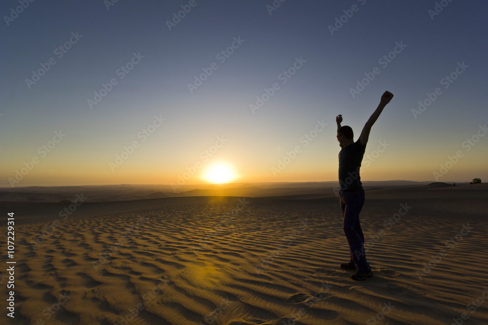 Fototapeta premium standing man with hands up at sunset in desert