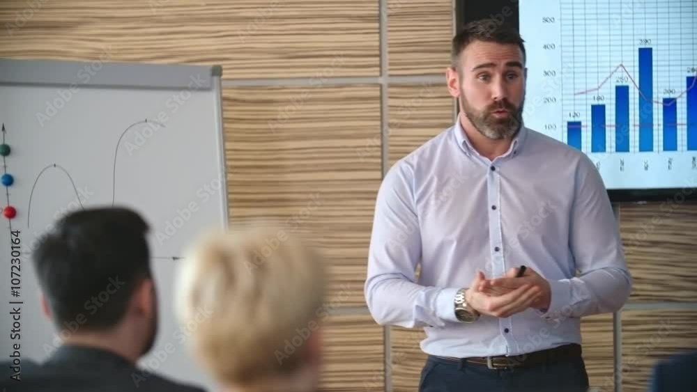 Mid-aged businessman standing in front of his colleagues and presenting financial bar graph on TV screen and flipchart