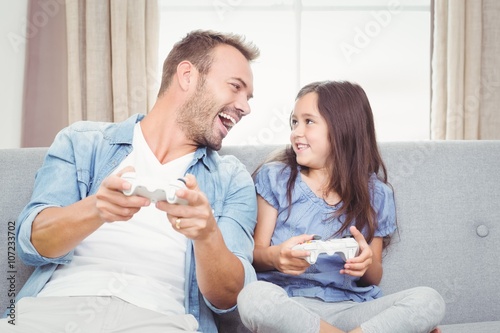 Smiling father and daughter playing video game 