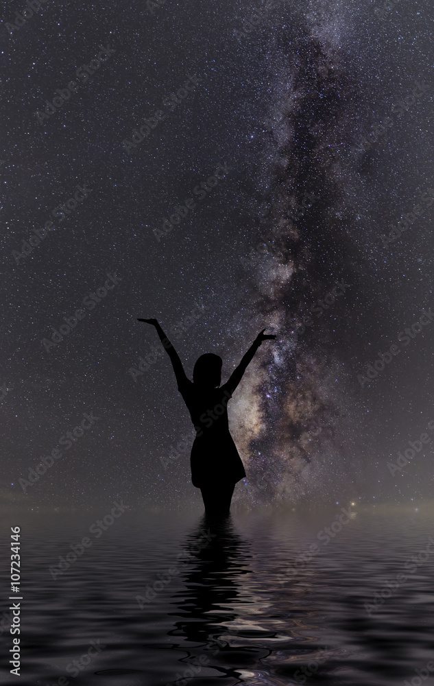 Fototapeta premium Silhouette of woman standing next to the milky way and pointing on a bright star.