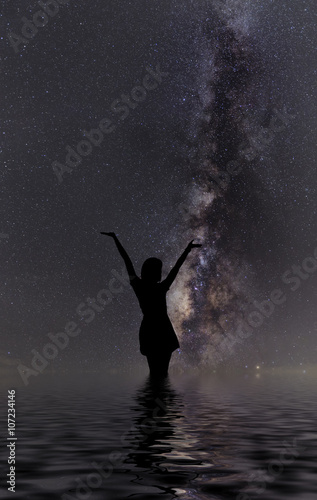 Silhouette of woman standing next to the milky way and pointing on a bright star.