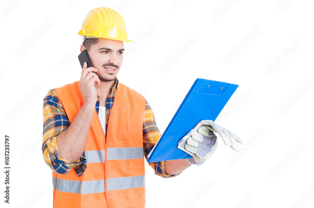 Young engineer wearing helmet with clipboard calling on cellphon Young engineer wearing helmet with clipboard calling on cellphon