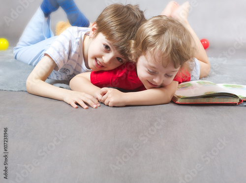 Two brothers 6 and 3 years old are hugging each other on a gray carpet. Free space for a text.
