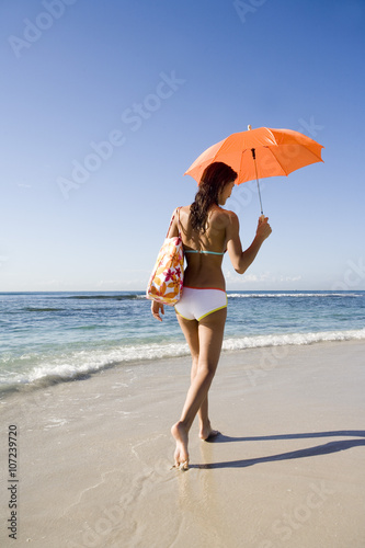 femme de dos en maillot de bain se promenant au bord de la mer avec une ombrelle orange  photo