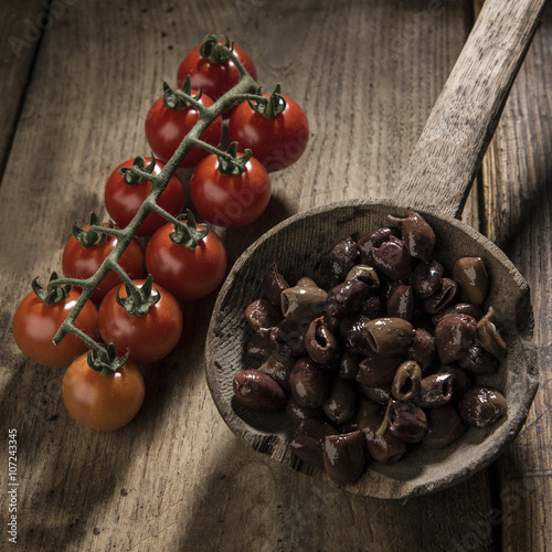 Olive snocciolate fatte in modo tradizionale su vecchio mestolo in legno con pomodorini ciliegiono e peperone - sfondo vecchio tavolo in legno photo