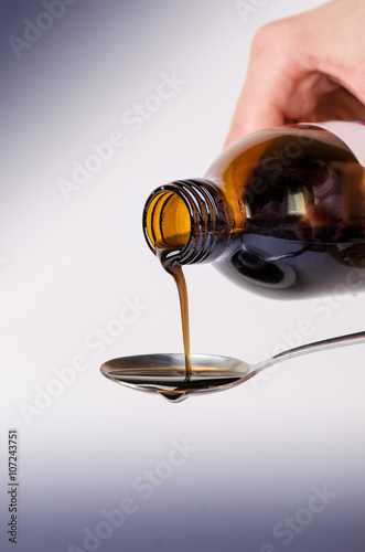 
    Bottle pouring a liquid on a spoon. Isolated on a white background. Pharmacy and healthy background. Medicine. Cough and cold drug. 