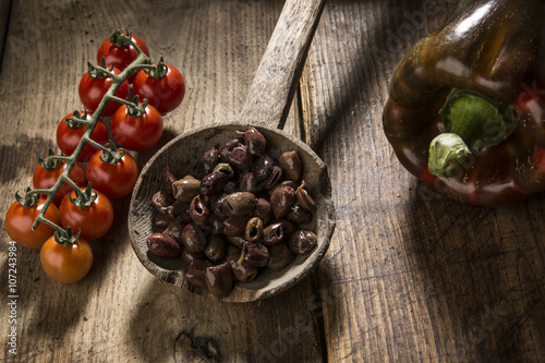 Olive snocciolate su vecchio mestolo in legno con pomodorini e peperone - sfondo vecchio tavolo in legno photo