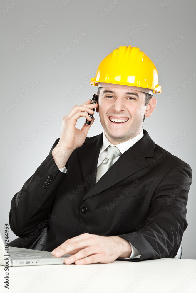 beautiful smiling engineer with yellow helmet and laptop talking on the phone isolated on grey beautiful smiling engineer with yellow helmet and laptop talking on the phone isolated on grey