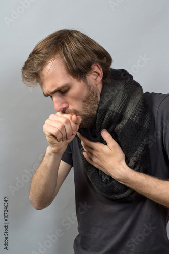 A man coughing into his fist. Gray background