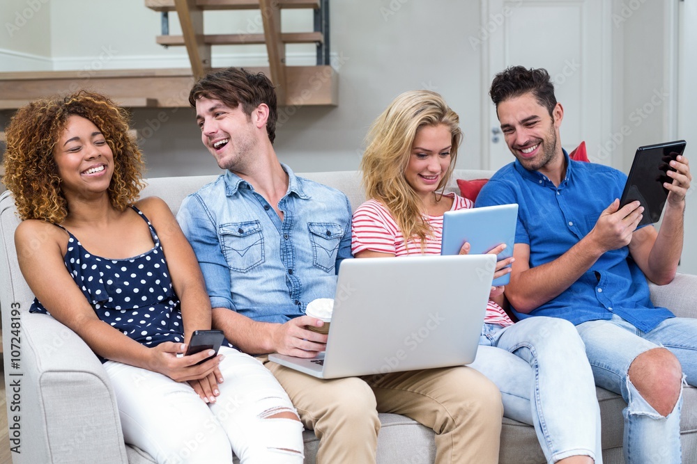 Friends smiling while using technologies at home Friends smiling while using technologies at home