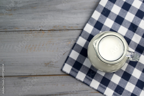 Milk in a glass jug on a wooden table, top view