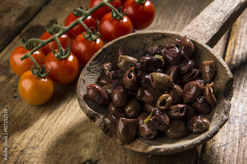 Olive snocciolate su vecchio mestolo in legno  e grappolo di pomodorini rossi - sfondo vecchio tavolo in legno photo