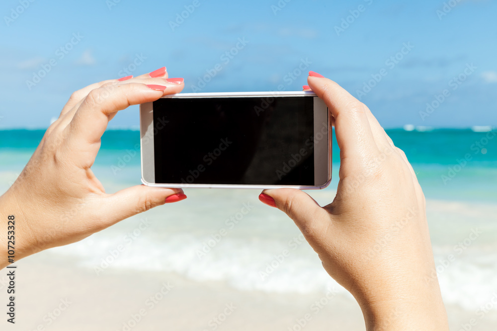 Woman holds phone for taking beach photo