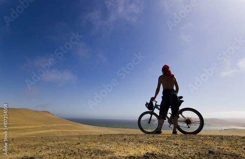 man standing with bicycle looking to ocean