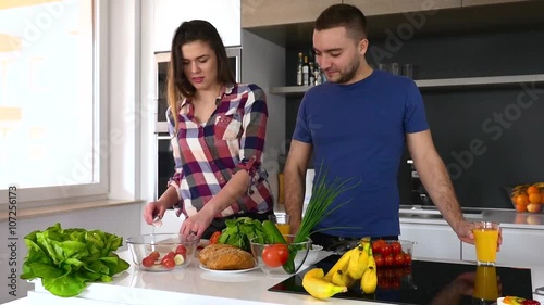 Young couple preparing saland in the kitchen. Man is drinking juice and huging woman.
 photo