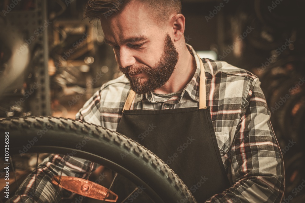 Stylish bicycle mechanic doing his professional work in workshop.