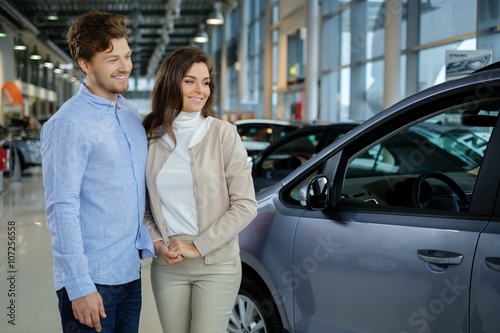 Beautiful young couple looking a new car at the dealership showroom.