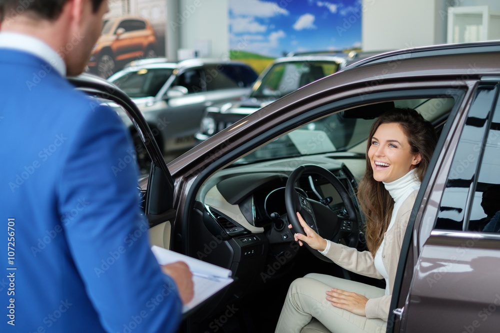 Beautiful young woman buys a car in the dealership saloon.