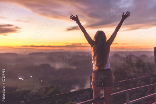 Silhouette of the woman spreading arms and standing high on the viewpoint with breathtaking view over fields in sunset light.Chocolate Hills, Bohol Island, Philippines.