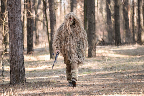 Soldier in camouflaged sniper suit  walking with gun/Soldier in camouflaged sniper suit  walking with gun in forest.Selective focus. photo