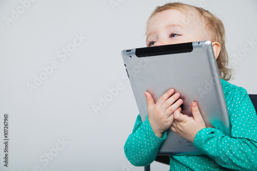 Infant child baby girl toddler sitting and typing digital tablet mobile computer isolated on a white background