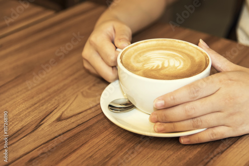 Hand holding coffee cup on wood table.