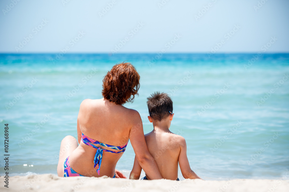 Back view of mother and son sitting on tropical beach Back view of mother and son sitting on tropical beach