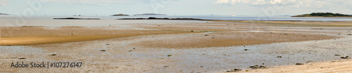 Panorama of a serene beach near Cramond Island, west of Edinburgh. Behind the yellow sand, we see islands in the Firth of Forth. A few boats in the distance add to the idyllic atmosphere.
