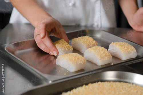 Fresh fish fillet cube covered in breadcrumbs, being placed onto a metal baking tray.