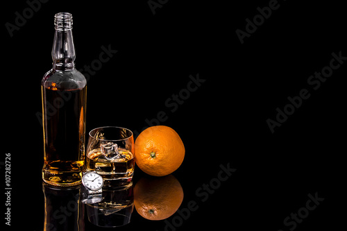 Bottle and glass whiskey with watch on black background