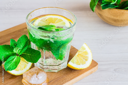 glass of cold water with fresh mint leaves, lemon and ice cubes