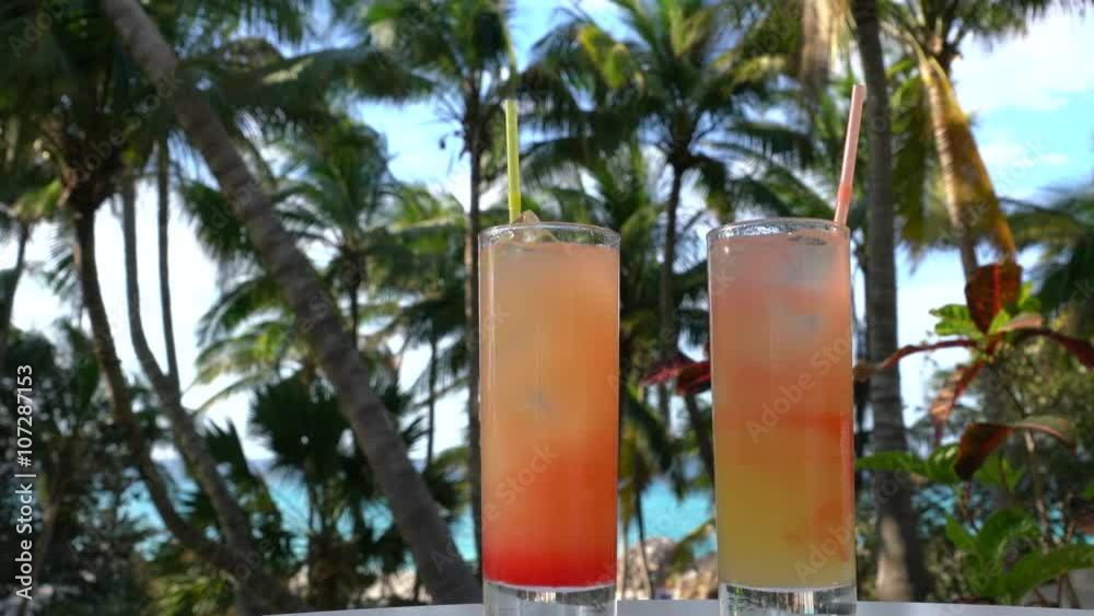 Cocktails stehen auf einem Tisch unter Palmen, Kamera verfolgt die Gläser von unten nach oben 
