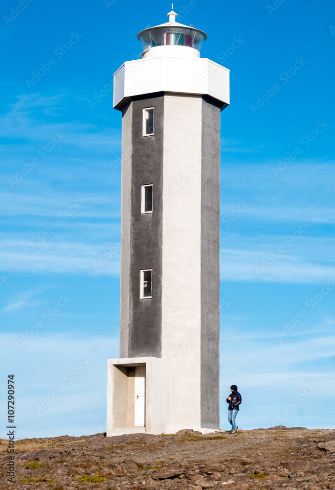 Grey lighthouse made of concrete with person walking next to it