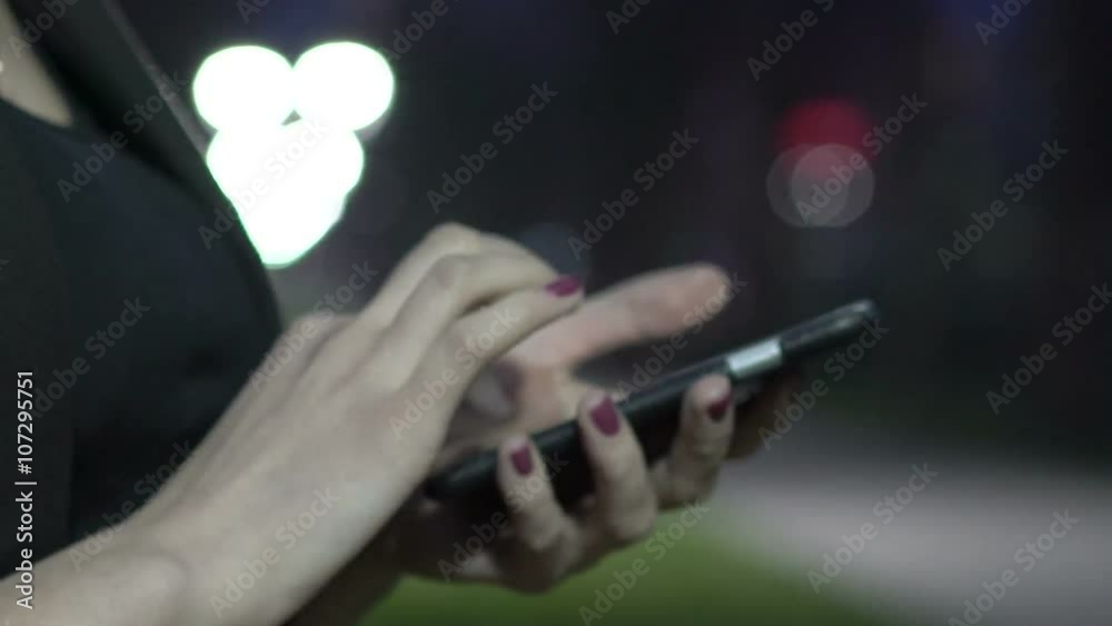 Young woman in the city at night typing on her touch screen smartphone