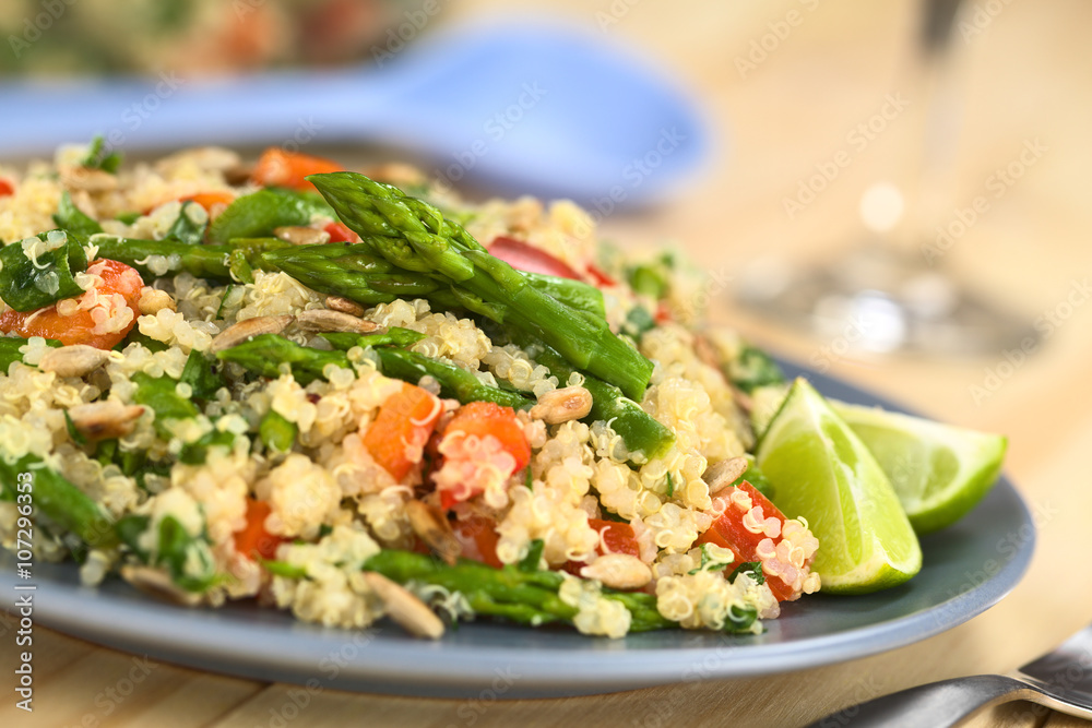 Vegetarian quinoa dish with green asparagus and red bell pepper, sprinkled with parsley and roasted sunflower seeds, lime wedges on the side (Selective Focus, Focus on the asparagus heads on the dish)