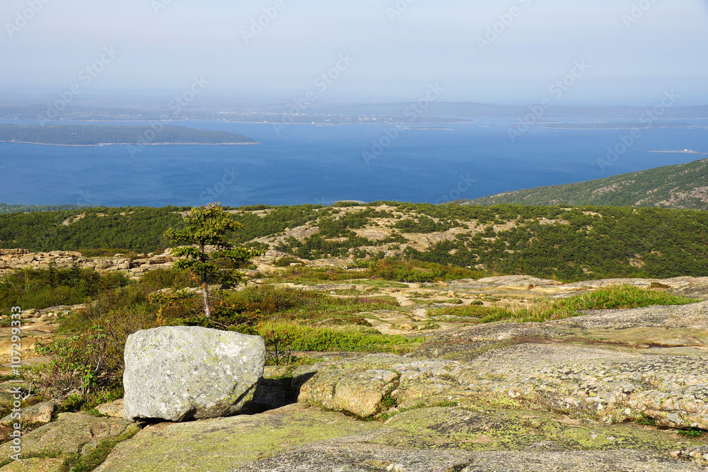 A bright day on the hilltop overlooking lake with islands with a boulder on the foreground.