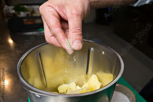 Close up shot of a hand dropping black pepper onto fluffy peeled potatoes into a blender.