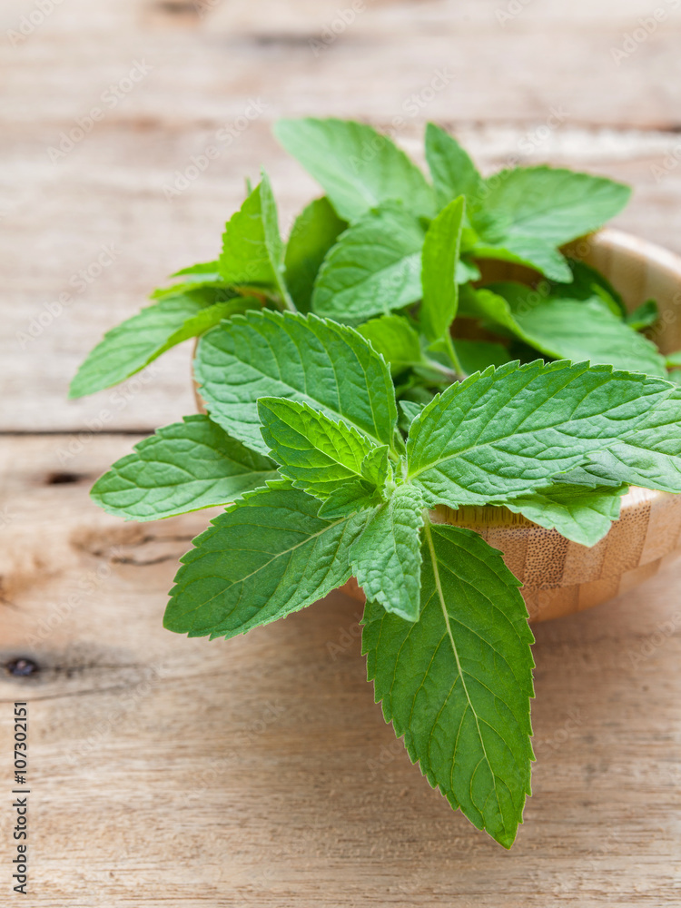 Closeup fresh peppermint leaves in the wooden bowl on rustic ta Closeup fresh peppermint leaves in the wooden bowl on rustic ta