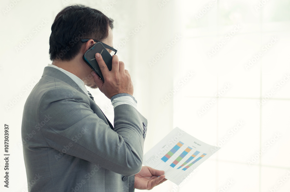 Asian businessman in grey suit speaking on the phone with docume Asian businessman in grey suit speaking on the phone with docume