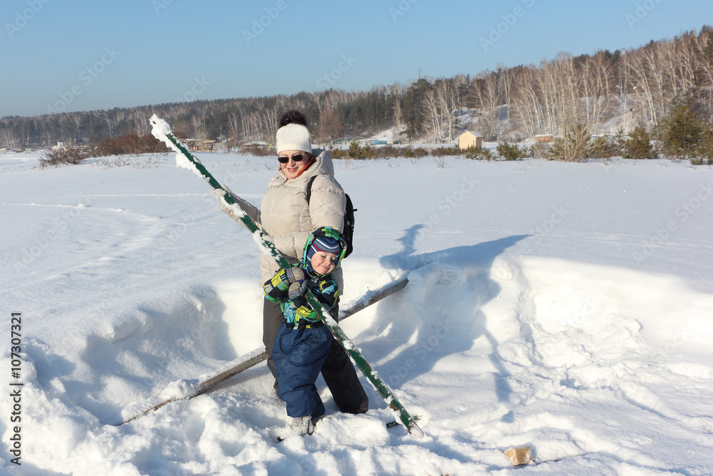 The woman and the kid in a color jacket playing with sticks on snow in the winter