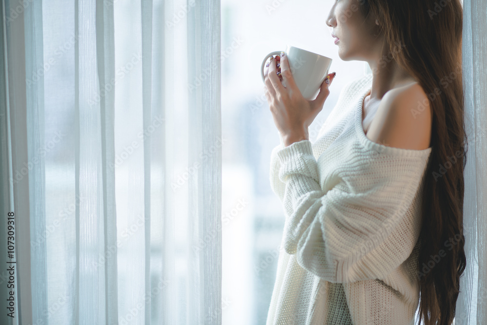 Fototapeta premium Cropped image of woman wit a big cup of coffee standing at window