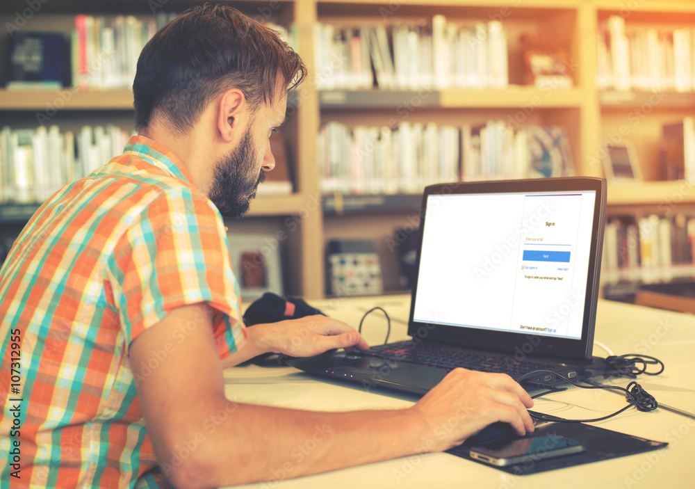 Side view shot of young business hipster man hands busy working on his laptop sitting at  table in a library with vintage filter effect
