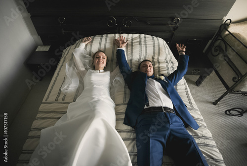 Happy bride and groom lying on bed at hotel room